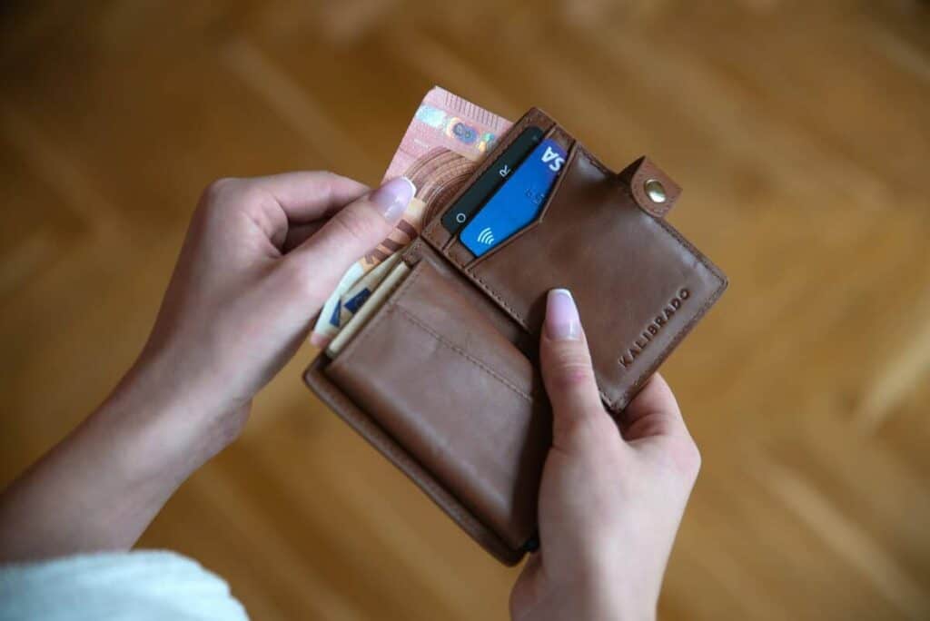 A person holds an open brown leather wallet containing euro banknotes and credit cards, carefully managing their finances.